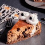 A slice of Halloween Cheesecake on a plate, topped with a whipped cream ghost and candy eyes.