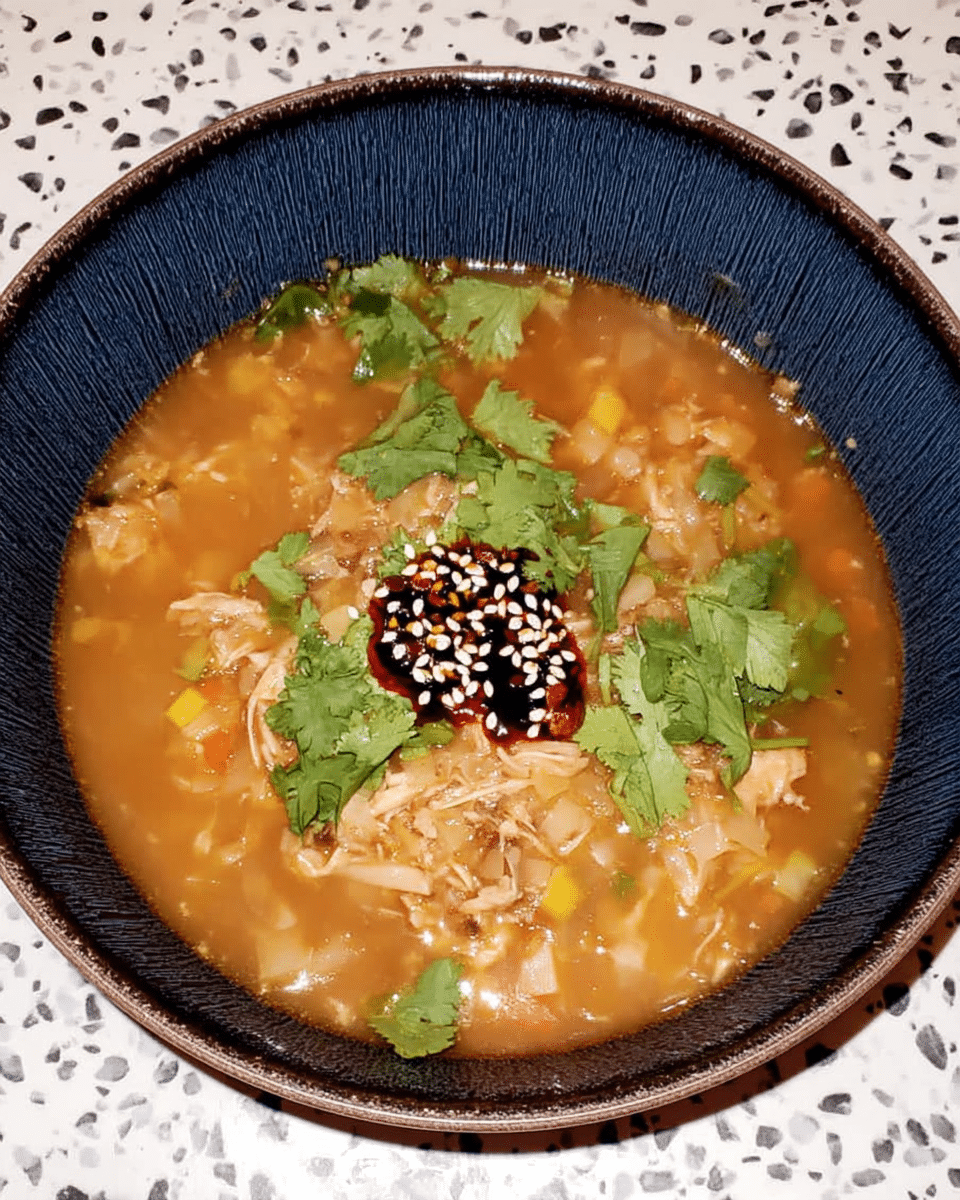 A steaming bowl of Lemon Chicken Orzo Soup, garnished with fresh parsley and lemon zest.