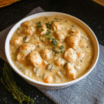A steaming bowl of Nourishing Pumpkin Wild Rice Soup (Vegan), garnished with fresh thyme, sits on a rustic wooden table.