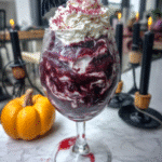 A close-up of two Vampire Bite Red Wine Milkshakes, topped with whipped cream and red sugar sprinkles, against a dark, moody background.