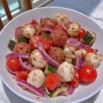 Cucumber Salad Caprese 7 Cucumber salad with mozzarella, tomatoes, and basil in a white bowl