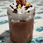 A tall glass filled with a black milkshake, topped with whipped cream and sprinkles.