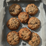 A close-up of a warm, chocolate chip cookie baked oat in a ramekin, topped with a splash of almond milk.