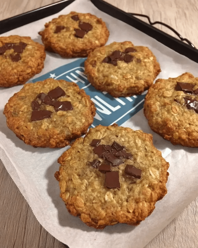 Chocolate Chip Cookie Baked Oats 9 A hand holding a spoon, adding a drizzle of honey to a serving of chocolate chip cookie baked oats.