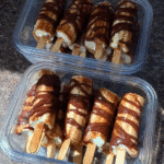 Frozen Chocolate Covered Banana Pops 7 A hand dipping a banana pop into melted chocolate, highlighting the smooth, glossy texture achieved by using coconut oil.