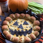 A close-up shot of the finished Halloween Buffalo Chicken Dip, garnished with ghost-shaped mozzarella cheese and spooky faces drawn with black writing gel.