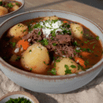 A steaming bowl of pot roast soup with chunks of beef, potatoes, and carrots, garnished with fresh parsley.