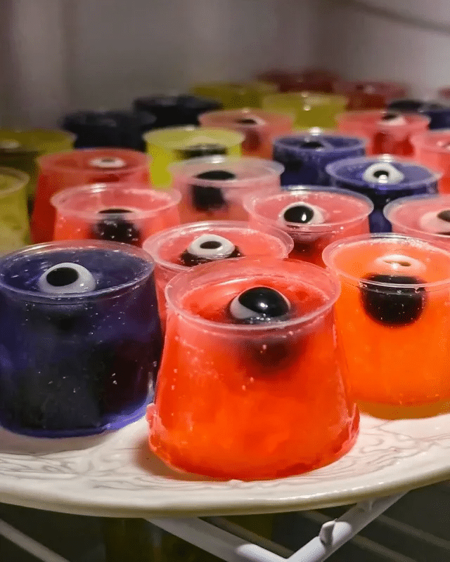 Halloween Eyeball Jello Shots 8 Ingredients for Halloween Eyeball Jello Shots arranged on a table: strawberry jello box, vodka bottle, candy eyeballs, and measuring cups.