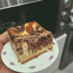 Close-up of a sliced No Bake Cheesecake Brownie on a plate, with a glass of milk in the background.