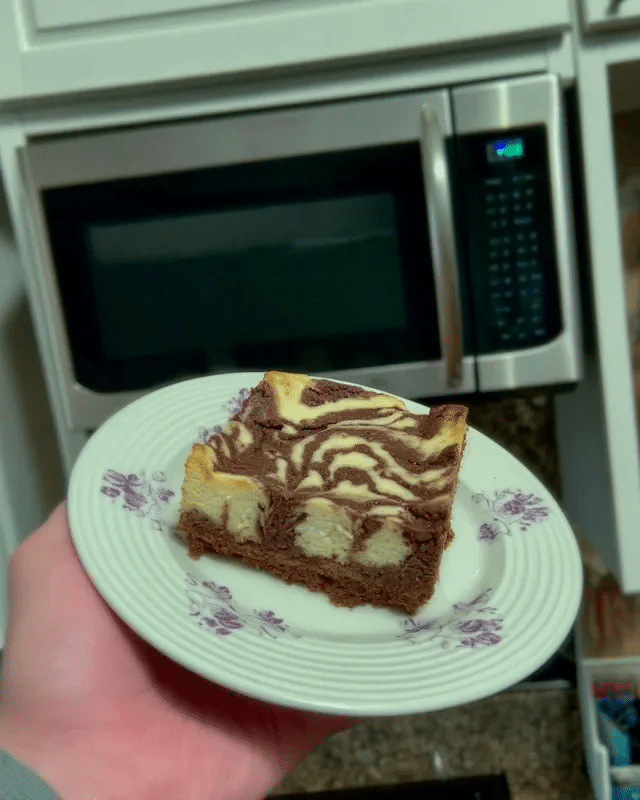 No Bake Cheesecake Brownies 9 A hand holding a knife dipped in hot water, demonstrating the tip of using a hot knife to slice the brownies cleanly.