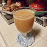 A glass of Poisoned Apple Cider garnished with blackberries and a cinnamon stick.