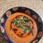 A bowl of vibrant Spicy Tomato Basil Soup garnished with fresh basil.