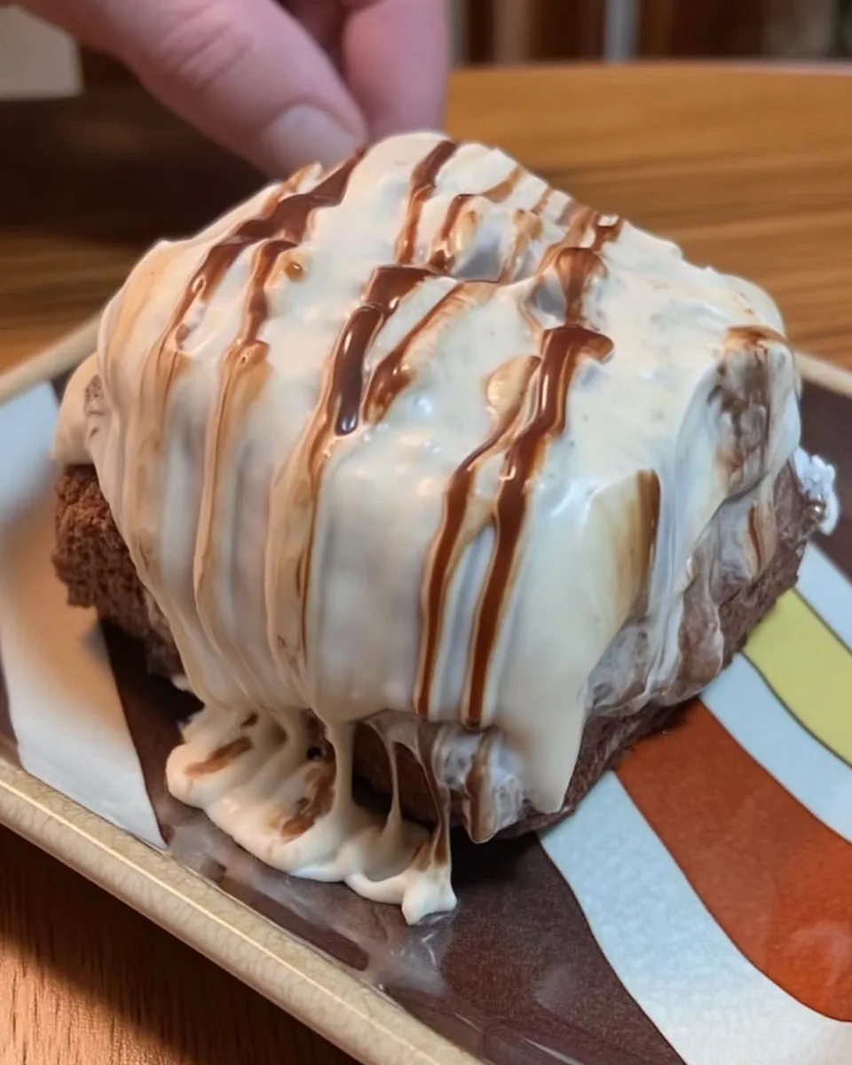 A slice of brownie refrigerator cake on a white dessert plate, showing the distinct layers of brownie, cream cheese, pudding, and whipped topping.